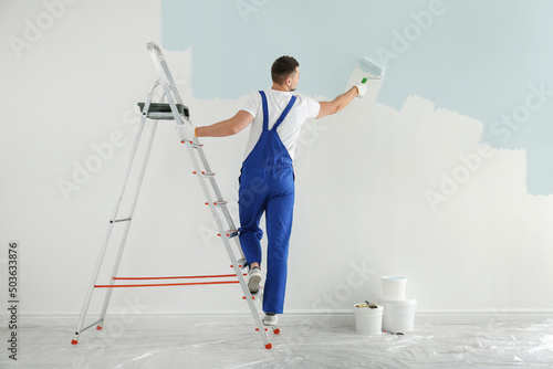 Man painting wall with light blue dye indoors, back view