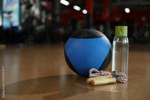 Medicine ball, bottle and skipping rope on floor in gym. Space for text