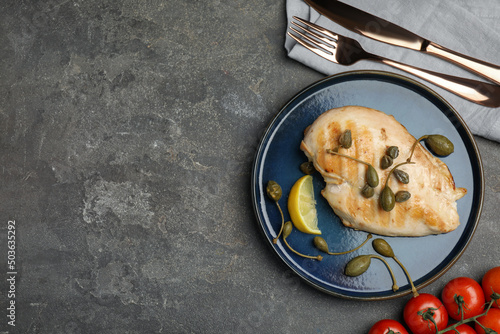 Delicious cooked chicken fillet with capers and lemon slice served on grey table, flat lay. Space for text