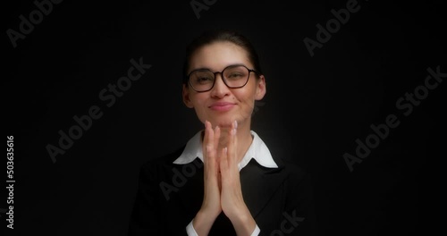 Cunning business woman in glasses and office clothes is standing on a isolated black background. Has evil plan in mind, steepled fingers, she came up with an idea