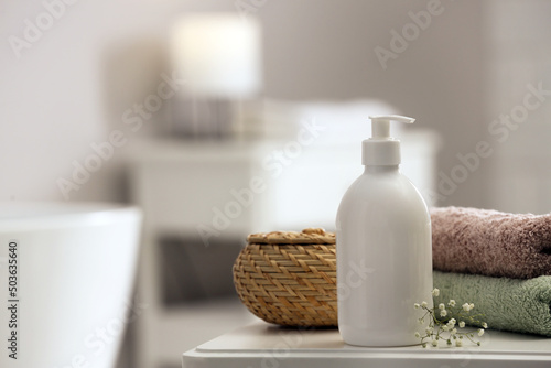 Bottle of bubble bath, towels, wicker box and flowers on white table in bathroom, space for text
