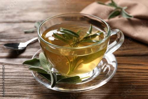 Cup of aromatic sage tea and fresh leaves on wooden table