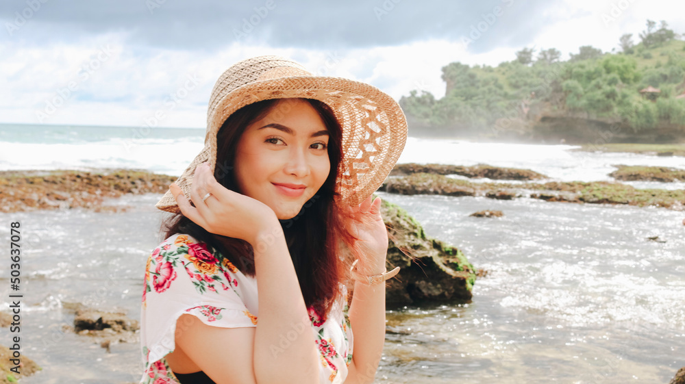 A young Asian girl wearing beach hat is relaxing on the blue sky beach at Gunungkidul, Indonesia