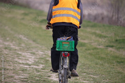 View from Behind of a Man on a Bicycle with a Reflective Jacket and a Green Basket Behind as a Luggage Carrier