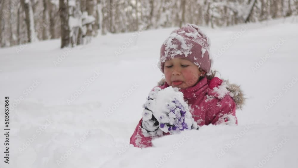 The little cute child girl is sitting in snowdrift at the forest and eating the snow with appetite, 4k The little cute child girl is sitting in snowdrift at the forest and eating the snow with appetite, 4k