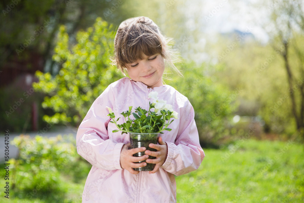 Fototapeta premium Spring awakening. Slow life. Enjoying the little things. Dreaming of spring. child with flowers in the garden. Child girl plant flowers in the garden near the houme on spring day.