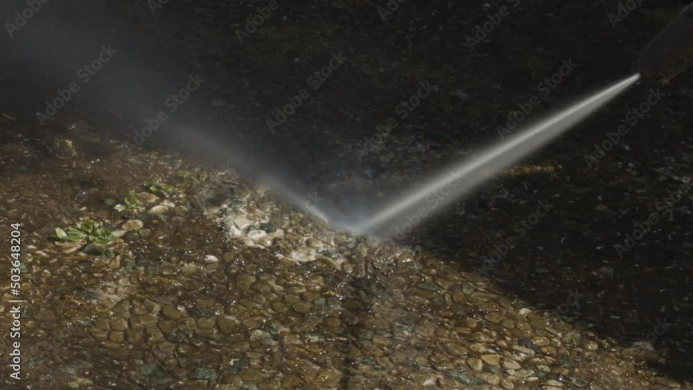 Powerful water jet from pressure washer being sprayed on weed and moss