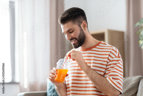 drinks and people concept - smiling man drinking orange juice with straw at home