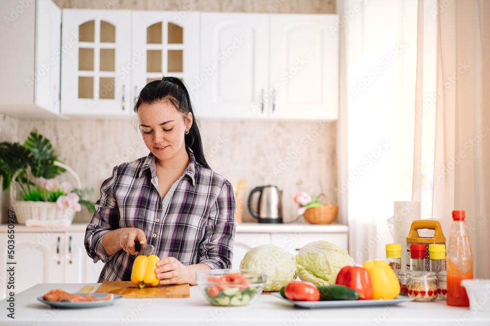A woman cooks healthy food in a bright kitchen. The concept of healthy nutrition with vitamins from vegetables to strengthen the immune system.