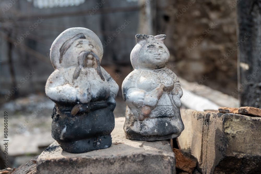 Figures of the traditional Ukrainian pottery school, the owner and mistress, a married couple against the backdrop of a destroyed and burned down house in Irpin, Ukraine Figures of the traditional Ukrainian pottery school, the owner and mistress, a married couple against the backdrop of a destroyed and burned down house in Irpin, Ukraine