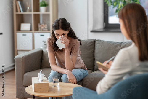 psychology, mental health and people concept - crying woman patient wiping tears with paper tissue and psychologist at psychotherapy session