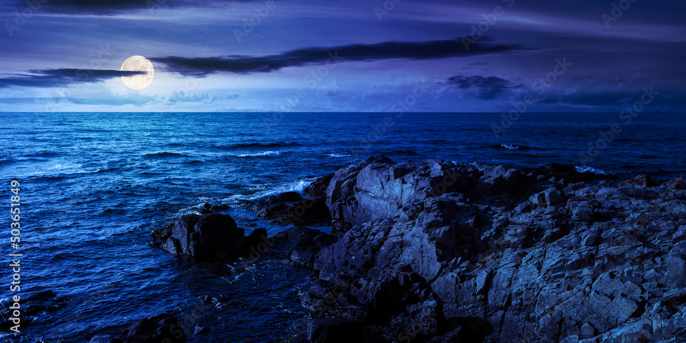 rocky sea coast at night. summer vacation concept. beautiful nature scenery with clouds on the blue sky above horizon in full moon light