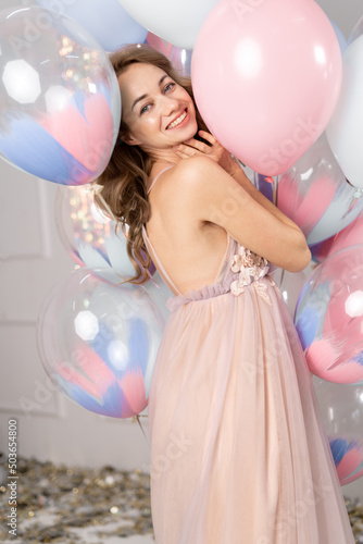 young happy blonde woman with balloons smiling, close-up, girl standing in a studio, laughing and playing with blue and pink baloons. She wears light dress and has braided hair. having fun.