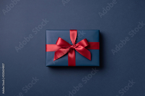 Blue gift box tied red ribbon on dark blue background. © Olga Zarytska