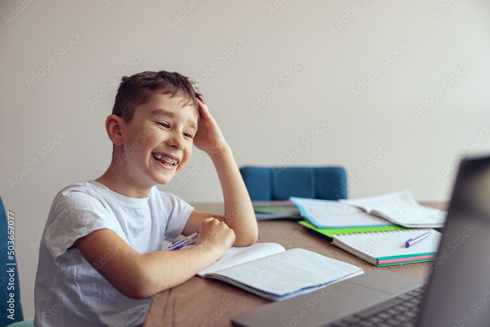 Cute cheerful little happy schoolboy with braces having online video lesson at laptop. Cute cheerful little happy schoolboy with braces having online video lesson at laptop.