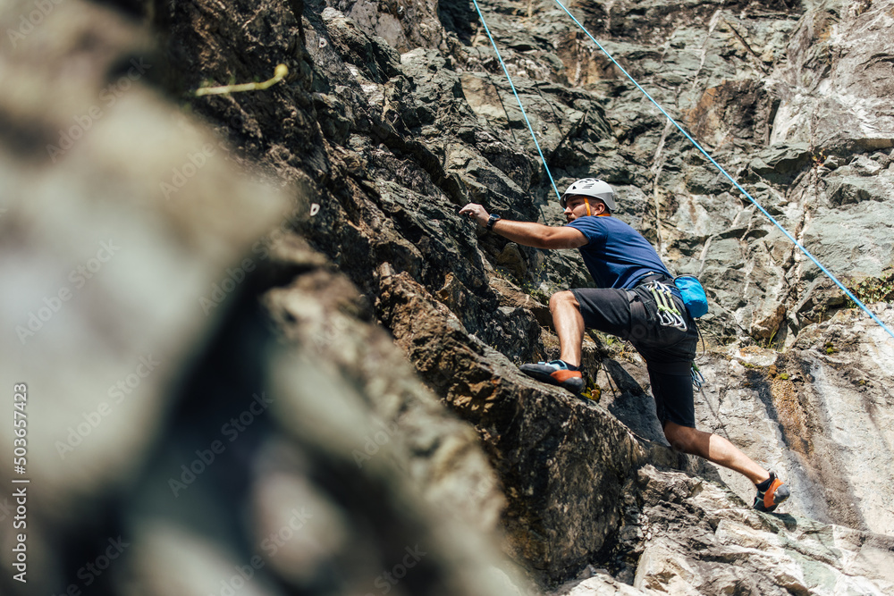 Side view of a strong man, climbing on the rock, wearing hamlet. Side view of a strong man, climbing on the rock, wearing hamlet.