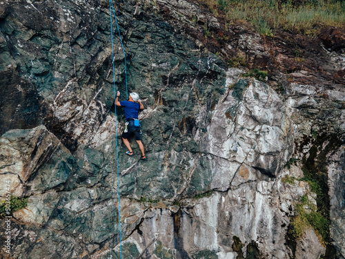 Photo of an adult male, using a rope as a help, climbing on the rock.