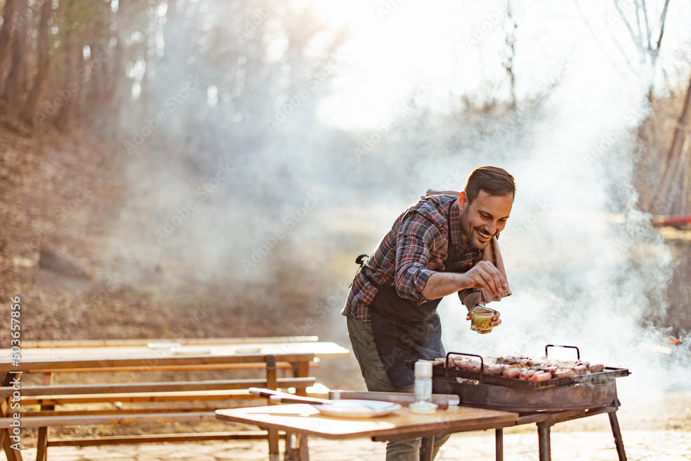 Man seasoning meat while making barbecue outdoors. Man seasoning meat while making barbecue outdoors.