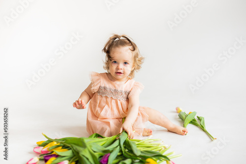 portrait of a little blonde girl with a bouquet of spring flowers on a light background. a child in a pink dress holds a bouquet of tulips in his hands. place for text. spring and summer concept. 