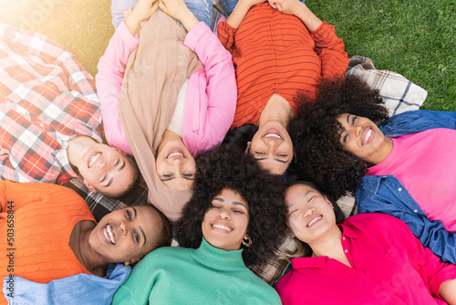 Multiracial women lying and smiling in the park of the friends enjoy the day to day together - millennials having a summer day at sunset in the city -