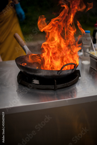 fire in the pan. Professional chef in a commercial kitchen cooking flambe style. Chef Flambe Cooking. Chef stir frys in wok. Dramatic cooking with fire hard photo