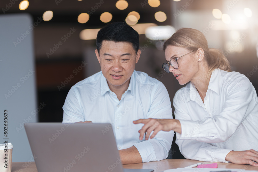 Fototapeta premium Two diverse business people focused while working on a laptop together at boardroom table in office.