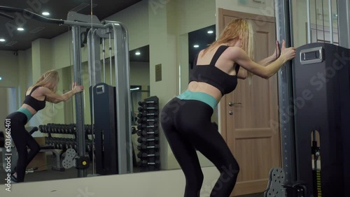 Woman performs an exercise for the muscles of the buttocks and legs in block simulator in the gym