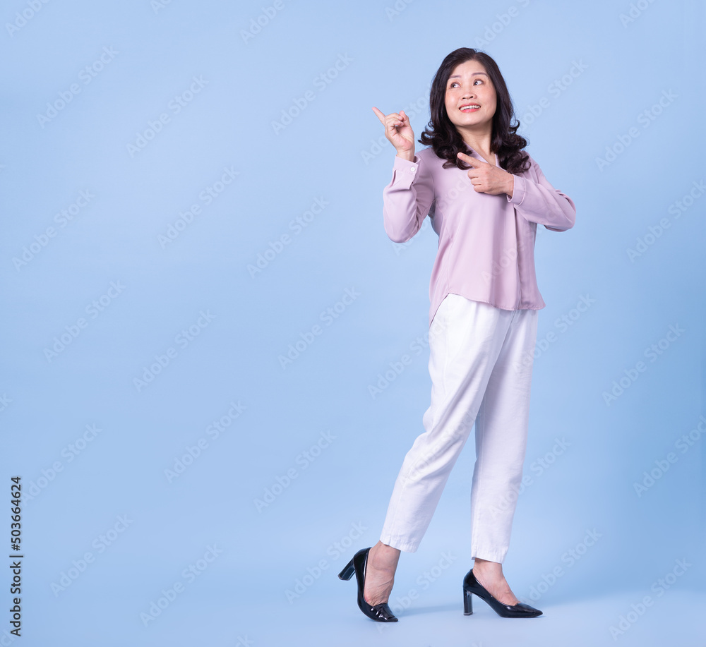 Full length image of middle aged Asian woman on blue background Full length image of middle aged Asian woman on blue background
