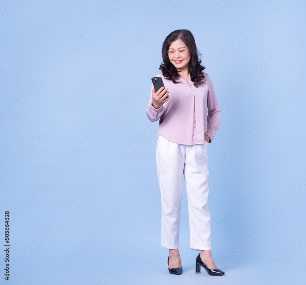 Full length image of middle aged Asian woman on blue background Full length image of middle aged Asian woman on blue background