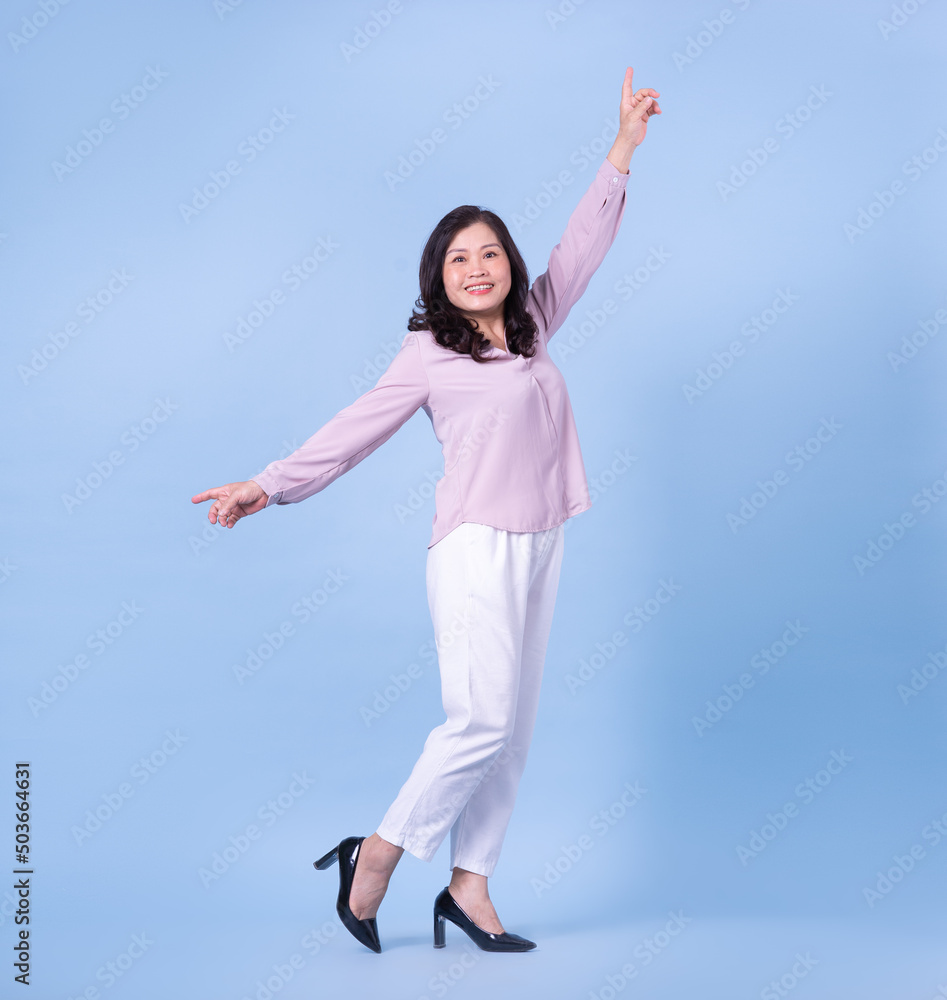 Full length image of middle aged Asian woman on blue background Full length image of middle aged Asian woman on blue background
