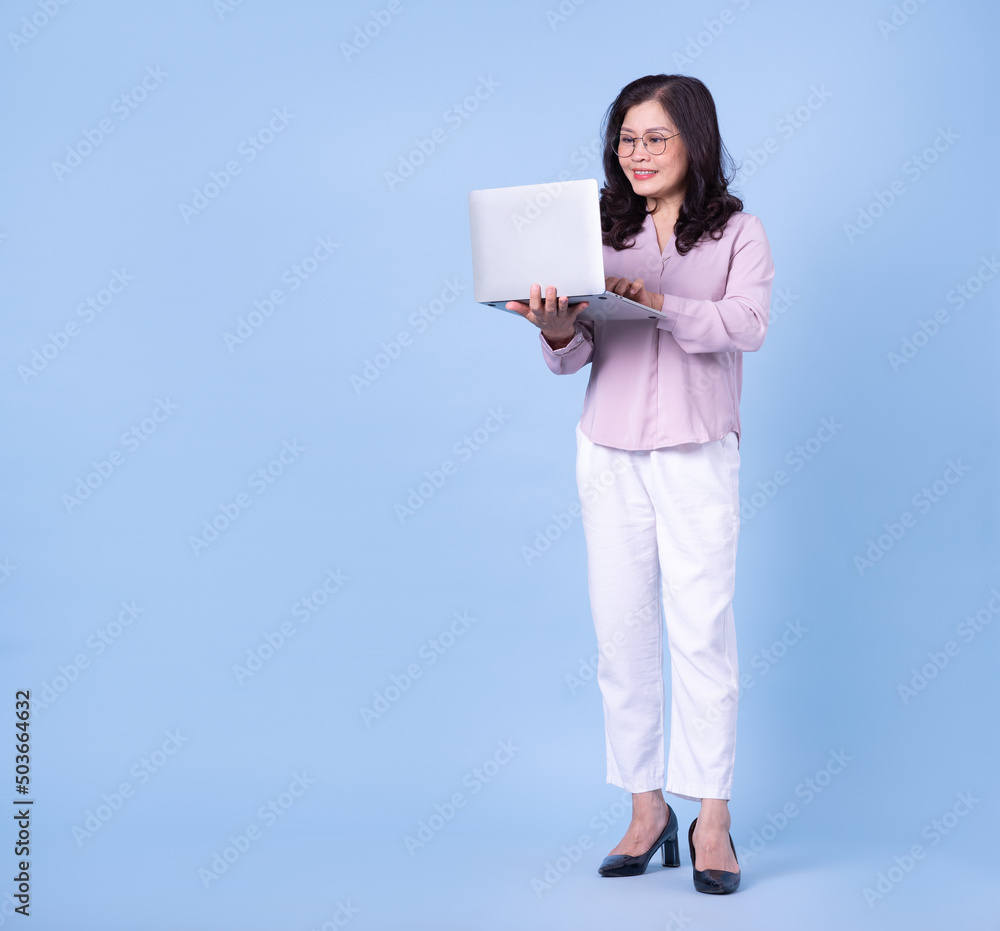 Full length image of middle aged Asian woman on blue background Full length image of middle aged Asian woman on blue background