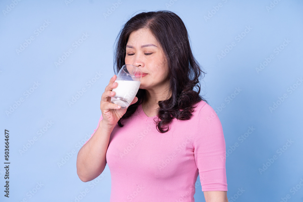 Image of middle aged Asian woman drinking milk on blue background Image of middle aged Asian woman drinking milk on blue background