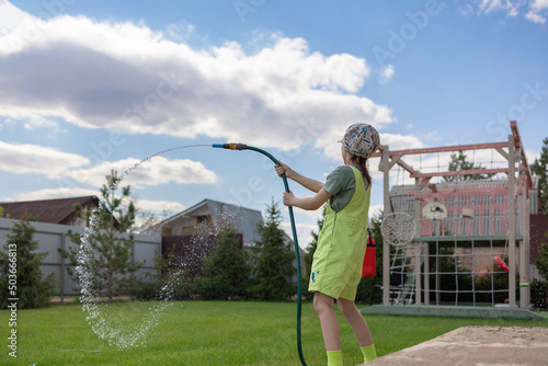 Little girl is watering seedlings from green watering can on spring sunny day. Work in garden. Country life. High quality photo