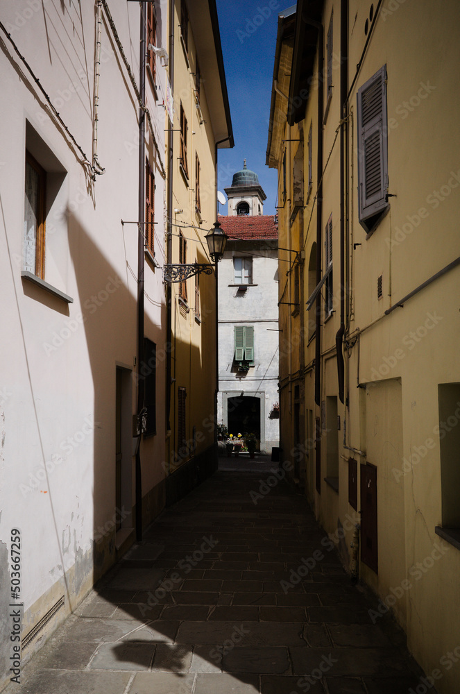 Narrow street in old town of Borgo Val di Taro, Parma province, Italy. Narrow cobbled street between old houses, town bell tower can be seen directly behind. Typical italian street in small town