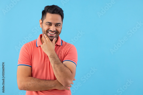 Portrait of a happy young man holding hand on chin and looking at camera against blue background