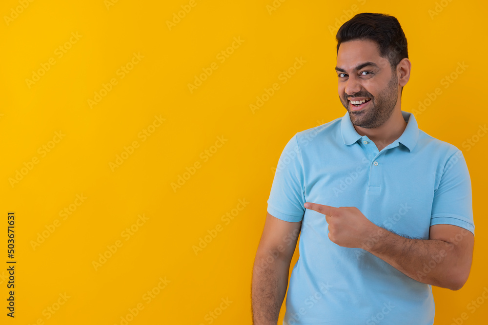 Smiling young man pointing sideways against yellow background Smiling young man pointing sideways against yellow background