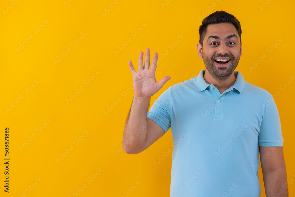 Portrait of a cheerful young man showing number with his fingers against yellow background