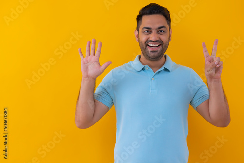 Portrait of a cheerful young man showing number with his fingers against yellow background