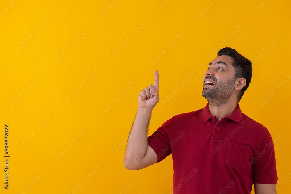 Portrait of a smiling young man pointing above against yellow background Portrait of a smiling young man pointing above against yellow background