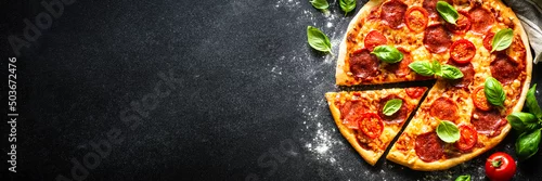 Obraz  z motywem Pizza on black background. Traditional italian pizza with salami cheese, tomatoes and basil. Long banner format good for web.