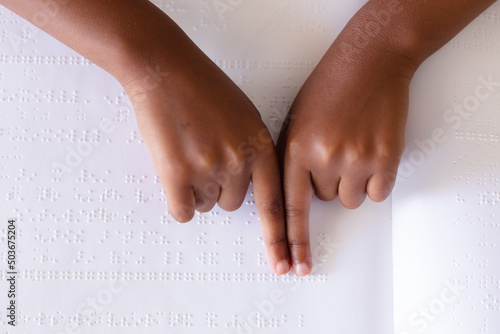 Cropped hands of african american elementary schoolgirl studying while touching braille book