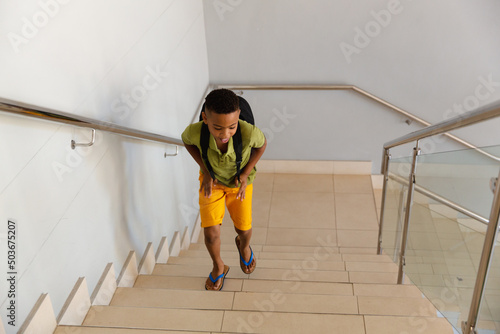 High angle view of african american elementary schoolboy with backpack climbing steps in school