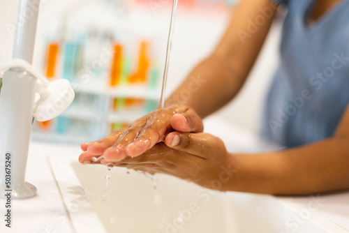 Midsection of biracial elementary schoolgirl washing hands in chemistry laboratory
