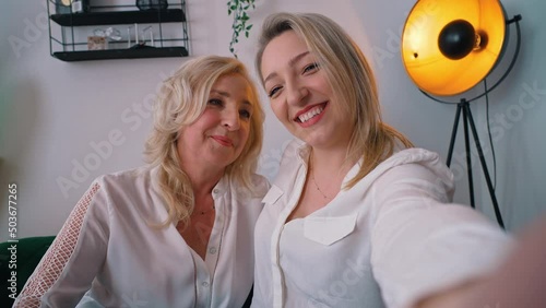 Indoor shot of two related caucasian women in their 40s wearing white elegant shirts takinga selfie, hugging each other and smiling. High quality 4k footage photo