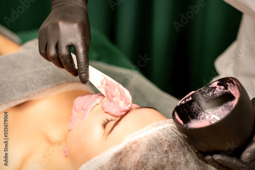 Beautiful young caucasian woman receiving an alginic mask to the face in beauty salon. Facial skin treatment photo