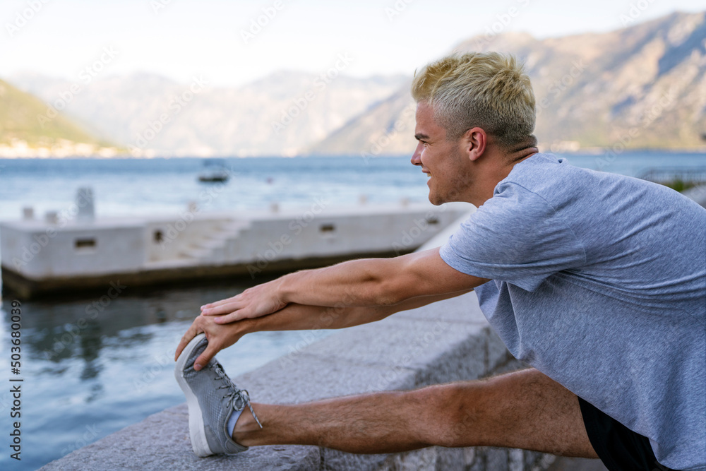Athletic male runner doing stretching exercise, preparing for morning workout outdoors Athletic male runner doing stretching exercise, preparing for morning workout outdoors