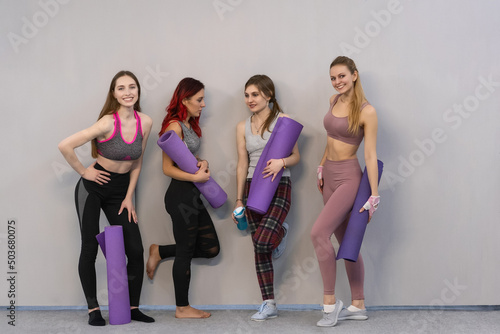 Group of young girls stand with yoga mats near the wall wearing sportswear waiting for the start of yoga or stretching classes. Sport concept