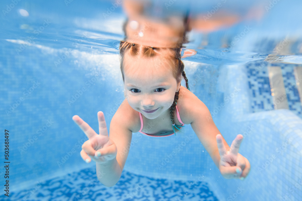 Little girl swims under water in paddling pool. Diving. Learning child to swim. Enjoy swimming and bubbles.