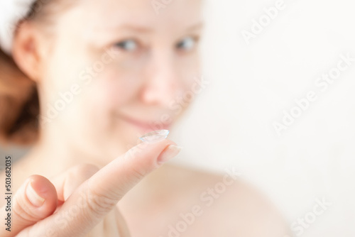 woman putting soft hydrogel contact lenses on her eyes on white background