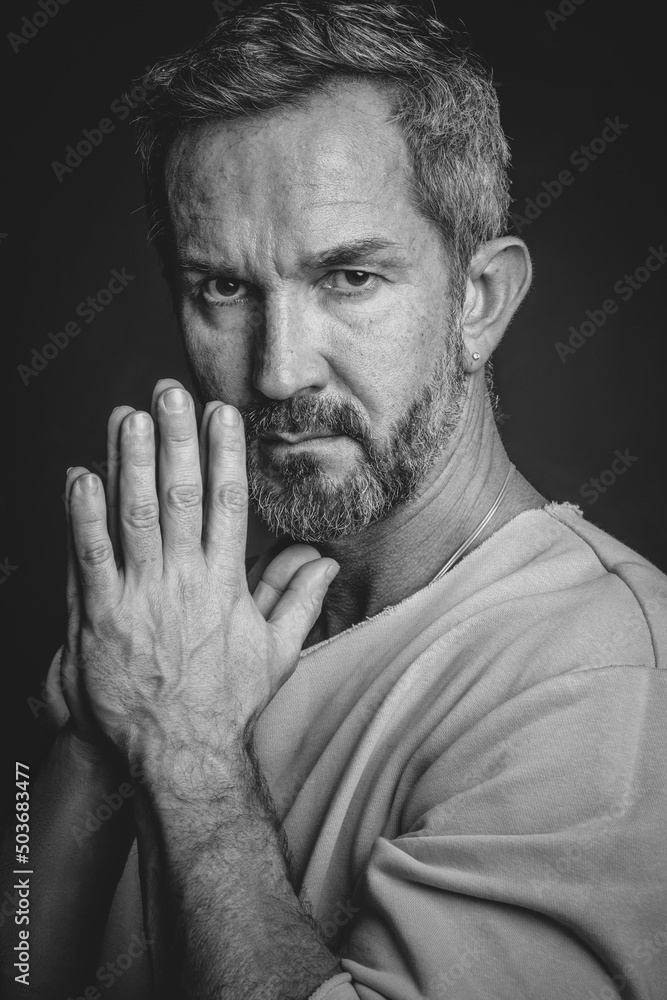 Grey haired mature man put hands together looking at camera. Handsome middle aged man in black and white photo. Black and white portrait of attractive, beautiful, serious man Grey haired mature man put hands together looking at camera. Handsome middle aged man in black and white photo. Black and white portrait of attractive, beautiful, serious man